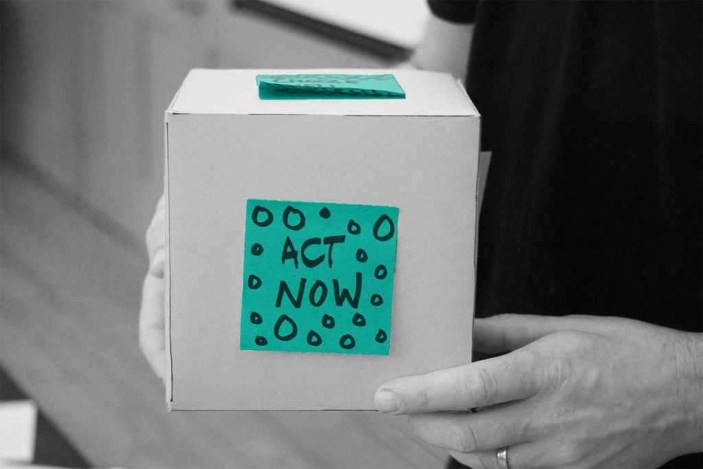 Box mit grünem Zettel, auf dem "Act now" steht