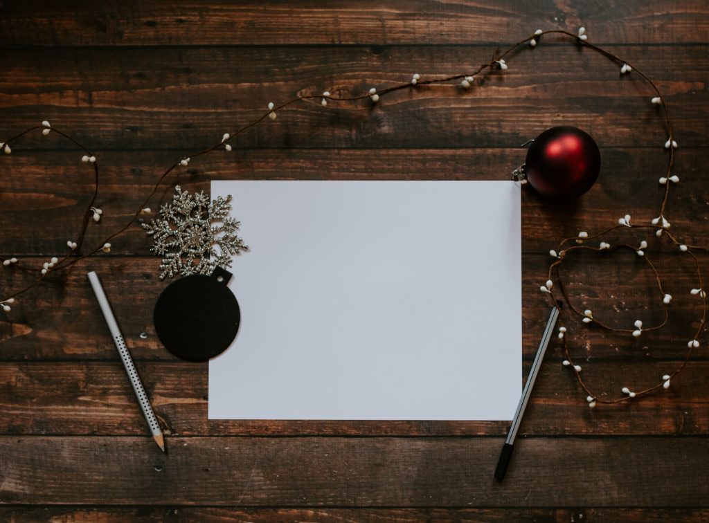 Ein festliches weißes Papier mit Weihnachtsdekorationen und Stiften auf einem Holztisch.