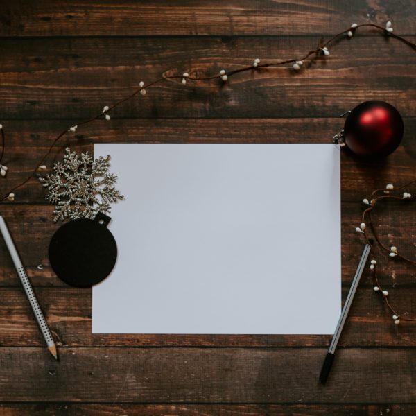 Ein festliches weißes Papier mit Weihnachtsdekorationen und Stiften auf einem Holztisch.