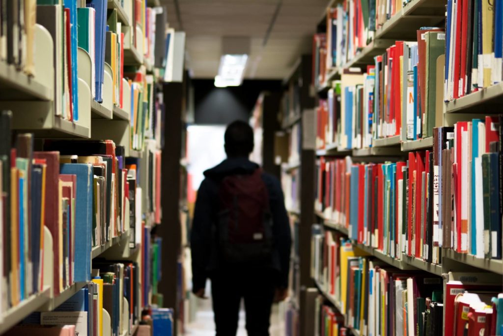 Ein Junge läuft mit dem Rücken zur Kamera durch die Bücherregale einer Bibliothek
